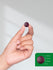 Hand holding a small purple object with a size reference on a green overlay.