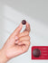 Hand holding a maroon circular object with a size measurement inset.