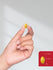 Hand holding a yellow pill with a red box inset showing dimensions.