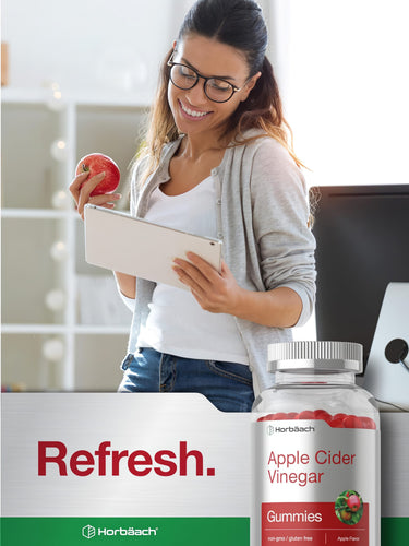 View 6 Young woman smiling, holding an apple and tablet, next to a bottle of Apple Cider Vinegar Gummies.