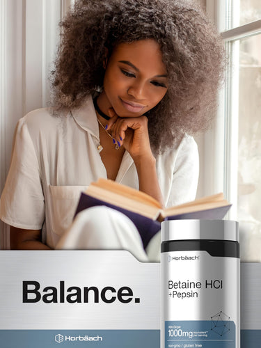 View 6 A young adult woman reads a book beside a bottle of Horbäach Betaine HCl + Pepsin.