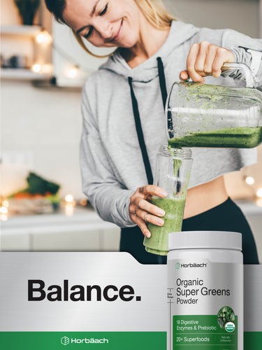 View 8 Lifestyle image of woman pouring a green smoothie into a glass with Horbäach Organic Super Greens Powder bottle nearby, stating Balance.