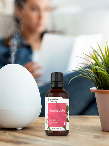 Bottle of Honeysuckle essential oil with a diffuser and plant on a table.