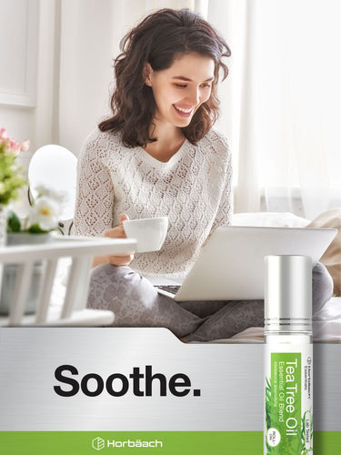 Woman sitting at a table with a laptop and cup, next to a bottle of Tea Tree Oil.