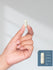 Hand holding a white capsule with a size reference on a gray background
